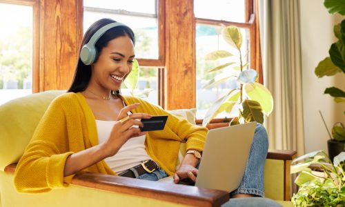 Happy woman, laptop and credit card with ecommerce and headphones to listen to music while online shopping. Female relax at home, radio streaming with fintech, internet banking and payment success.